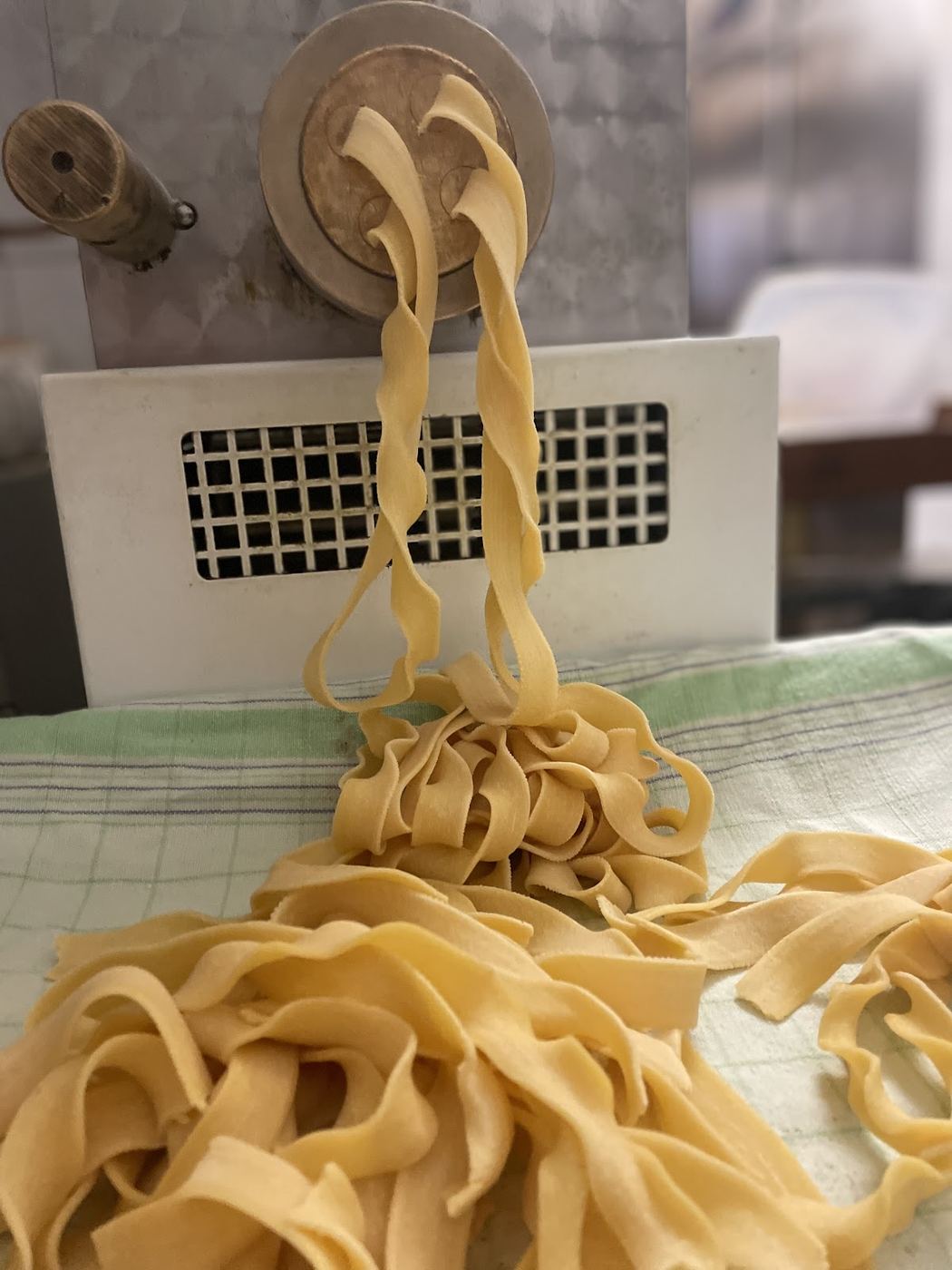 Pappardelle fresche che escono dalla macchina della pasta e si posano su un canovaccio