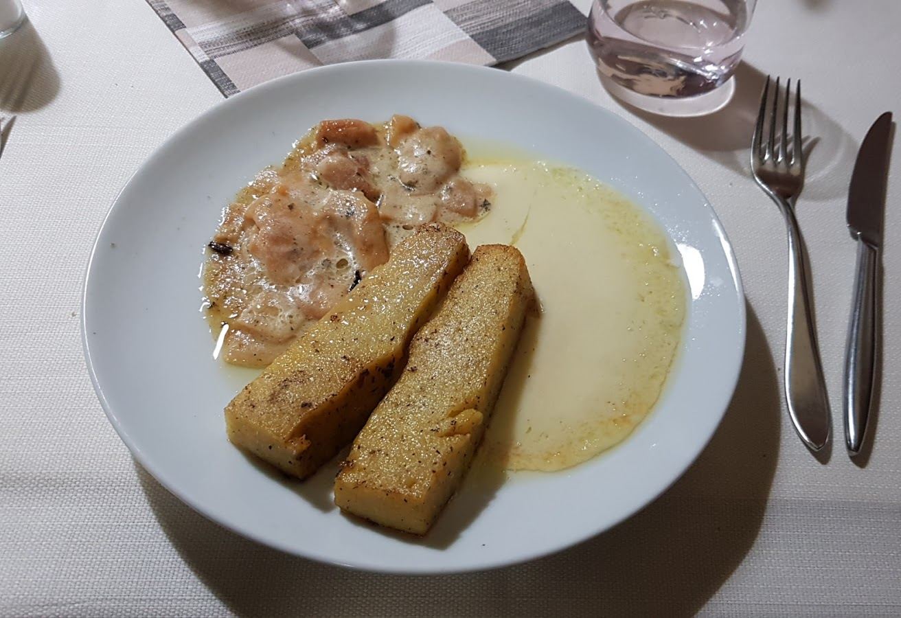 Due fette di polenta abbrustolita con formaggio fuso e un sugo cremoso, in un piatto bianco